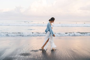 Muhteşem beyaz kadın plajda sakin ve kaygısız bir şekilde yürürken tatilin tadını çıkarıyor. Beyaz yaz giysileri içinde güzel, sağlıklı bir kadın tatil boyunca deniz kıyısında gezer.