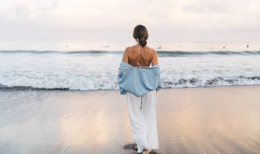 Muhteşem beyaz kadın plajda sakin ve kaygısız bir şekilde yürürken tatilin tadını çıkarıyor. Beyaz yaz giysileri içinde güzel, sağlıklı bir kadın tatil boyunca deniz kıyısında gezer.