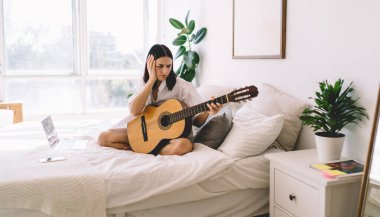 Esmer kadın gitar çalamadığı için üzgün. Genç kadın baş ağrısı yüzünden müzik aletleriyle hobi yapamıyor.