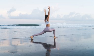 Sahil şeridinde sabah antrenmanı sırasında bacakları ve vücut kaslarını esneten beyaz kadın yogi 'nin yan görüntüsü. Hatha Asana' da deniz kıyısında duran esnek eşofmanlı kadın.