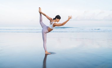 Kafkasyalı kadın, vücut şekli iyi Hatha Asana pozuna yoğunlaşmış, bacağı kalkmış, spor eşofmanlı genç bayan deniz kıyısı inzivasında bütünsel iyileşme sırasında canlılık için esniyor.