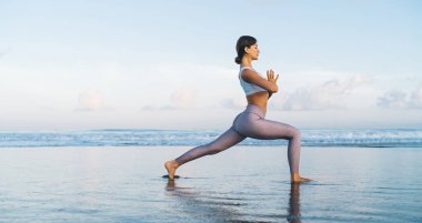Harika bir kadın hafta sonu boyunca yoga yapıyor kıyı şeridinde egzersiz yapıyor Asana 'da, Kafkasyalı bir kadın aydınlanma peşinde meditasyon yaparak hatha rutini yapıyor.
