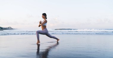 Esnek formda bir kız, sabah vakti okyanus kenarında egzersiz yapmak için yoga yapıyor sağlıklı bir kadın bacaklarını esneterek sağlıklı yaşam ve yaşam tarzını koruyor.