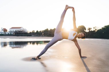 Esnek bayan sporcu, sabah pilates antrenmanı sırasında kaslarını esneten okyanus kenarında spor kıyafetleri giymiş, vücudu ve sağlıklı yaşam tarzını korumak için yoga asanası yapan beyaz kadın.