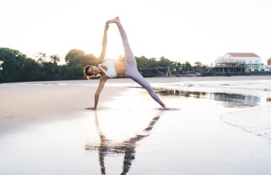 Modayı takip eden sportif giyinen sakin bir kadın. Kıyı şeridindeki yoga eğitimi sırasında dinleniyor. Uyum ve dengeyi hissediyor.