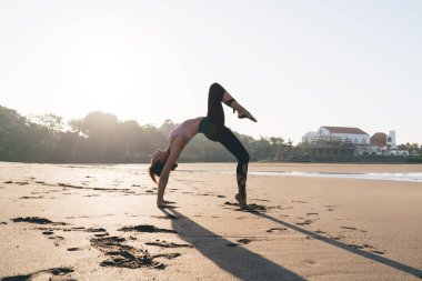 Deniz kenarında sabah güneşinde hatha egzersizi yapan esnek kadın yogi. İnce vücut kaslarını esneterek kıyı şeridindeki pilates eğitiminde doğadan ilham alan sağlıklı kız.