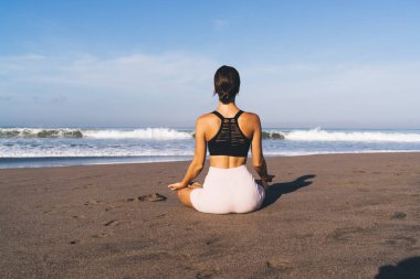 Kıyı şeridindeki Lotus 'ta otururken Zen Bilinci' ni düşünen dişi yogi 'nin arka planda kalan görüntüsü. Sabah antrenmanı sırasında eşofmanlı kadın meditasyon sırasında uyum arayışı için dinleniyor.