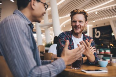 Geniş ofisteki masada konuşan ve içki içen çok ırklı işadamları. Dinlenme ve işten ayrılma kavramı. Modern ve başarılı insanların fikirleri. Genç Asyalı ve Avrupalı erkekler birbirlerine bakıyorlar.