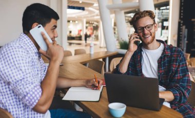 Ofiste çalışırken akıllı telefonlardan konuşan çok ırklı iş adamları. İş birliği ve takım çalışması kavramı. Modern ve başarılı insanların fikirleri. Masada oturan Asyalı ve beyaz adamlar.