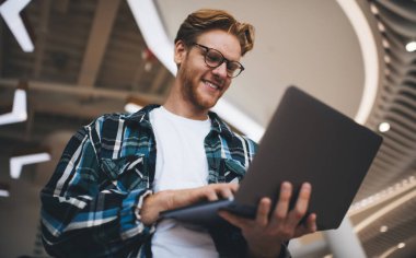 Kafkasyalı adamın dizüstü bilgisayarında daktilo edişinin alt görüntüsü. Uzaktan eğitim ve iş kavramı. Modern, başarılı bir adamın fikri. Gözlüklü genç adam geniş ofiste çalışıyor ya da çalışıyor.