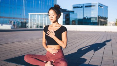 Sakin Asyalı kadın gündüz vakti şehir merkezinde pranayama için dua etmeye devam ediyor. Eğlencenin tadını çıkartıyor, genç bayan yogi Lotus 'ta meditasyon yapıyor. Ruhunu aydınlatmak ve sakinleştirmek için arayış içinde.