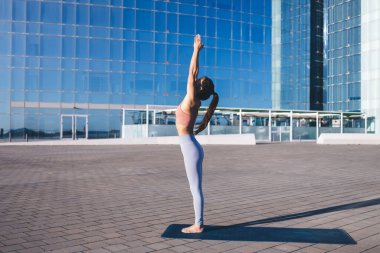 Eşofmanlı, vücut kaslarını geren, kentte ısınma egzersizleri yapan genç bir Yogi, spor giyim konusunda esnek Asyalı bir kadın zindelik ve sağlıklı yaşam tarzına erişiyor.