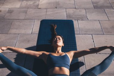 Sıradan giyinen, siyah mindere uzanan, yoga yapan, vücut bakımına özen gösteren, sabah antrenmanlarından zevk alan, iç huzuru hissetmek için asana pozları veren genç bir kadın.