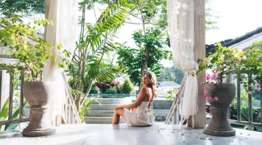 Otelin merdivenlerinde oturup dinlenen heyecanlı genç bir kadın. Turizm, tatil ve hafta sonu kavramı. Güneşli bir gün. Çekici Avrupalı kız. Bali adasında huzurlu ve huzurlu bir yaşam tarzı