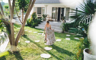 Güneşli bir günde otelin bahçesine gülümseyen genç bir kadın. Turizm, tatil ve hafta sonu. Elinde deniz kabuğu ve tütsü çubuğu tutan beyaz elbiseli güzel bir kız. Idyllic ve sakin yaşam tarzı