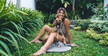 Otelin bahçesinde sevimli köpeğe sarılan mutlu genç bir kadın. Turizm, tatil ve hafta sonu. Sahibi ve evcil hayvan ilişkisi ve dostluğu. Beyaz kız kameraya bakıyor. Idyllic ve sakin yaşam tarzı