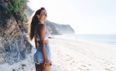 Neşeli bayan turist yaz tatillerinde ve deniz kıyısında eğleniyor. Yüzünde samimi bir gülümsemeyle uluslararası sahil şeridinde dinlenmek için seyahat etmekten memnun olan Kafkasyalı kadın.