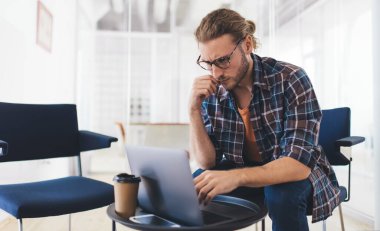 Milenyum Kafkas işadamı dizüstü bilgisayardan izliyor. Modern başarılı adam kavramı. Gözlüklü genç girişimci ofisteki ofis koltuğunda oturuyor ve çalışıyor.