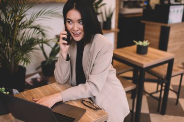 Kafede dizüstü bilgisayarla çalışırken Asyalı iş kadını akıllı telefondan konuşuyor. Genç, güzel, bin yıllık esmer kadın masada oturuyor. Serbest çalışma ve uzak çalışma kavramı. Modern kadın yaşam tarzı