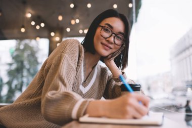 Not defterine yazı yazan Asyalı bir kız ve kafede kameraya bakıyor. Bin yıllık gülümseyen esmer kadın pencerenin yanındaki masada gözlük takıyor. Dinlenme, boş zaman ve boş zaman. Modern kadın yaşam tarzı