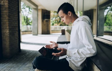 Yoğunlaştırılmış erkek uzaktan işçinin modern dizüstü bilgisayardan bilgi okuyup iş sırasında el sallamasının yan görüntüsü