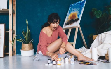 Çekici genç bayan ressam resim çiziyor ve hobisinin rahatlatıcı sürecinden zevk alıyor. Yaratıcı ve yetenekli esmer kadın stüdyoda resim yapıyor. Petrolle çizim yapmayı öğrenmek