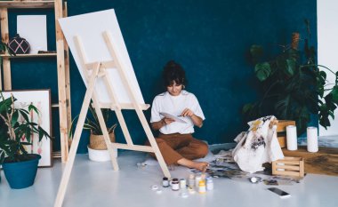 Çekici genç bayan ressam resim çiziyor ve hobisinin rahatlatıcı sürecinden zevk alıyor. Yaratıcı ve yetenekli esmer kadın stüdyoda resim yapıyor. Petrolle çizim yapmayı öğrenmek