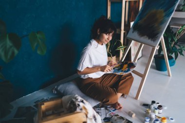 Çekici genç bayan ressam resim çiziyor ve hobisinin rahatlatıcı sürecinden zevk alıyor. Yaratıcı ve yetenekli esmer kadın sehpada resim yaratıyor. Petrolle çizim yapmayı öğrenmek