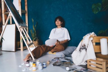 Çekici genç bayan sanatçı stüdyo zemininde oturmuş hobisinin keyfini çıkartıyor. Yaratıcı ve yetenekli esmer kadın sehpada resim yaratıyor. Petrolle çizim yapmayı öğrenmek