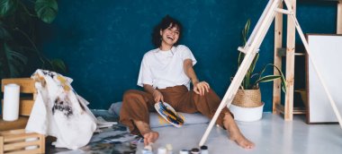 Heyecanlı genç bayan sanatçı stüdyo zemininde oturmuş, resimleriyle hobisinin tadını çıkarıyor. Yaratıcı ve yetenekli esmer kadın sehpada resim yaratıyor. Petrolle çizim yapmayı öğrenmek