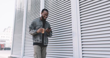 Şehirde gülümseyen mutlu siyah turist seyahat sırasında GPS 'i takip etmek için hücresel uygulama kullanıyor, optik göz giysisi giyen neşeli hippi adam çevrimiçi ağ kurmaktan ve sohbet etmekten hoşlanıyor.