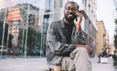 Klasik gözlüklü mutlu koyu tenli adamın portresi. Şehir merkezinde hücre sohbeti yaparken kameraya bakıyor. Gözlüklü Afro-Amerikan hippi adam cep telefonu teknolojisiyle arıyor.