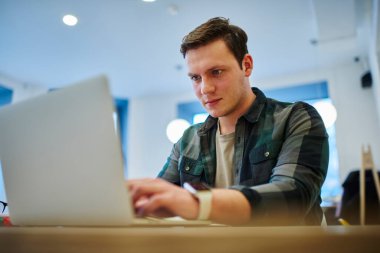 Genç düşünceli bir adam internette çalışırken dizüstü bilgisayarı başında oturuyor. Erkek öğrenci netbook ile öğreniyor. Web sitesinde makale okunuyor