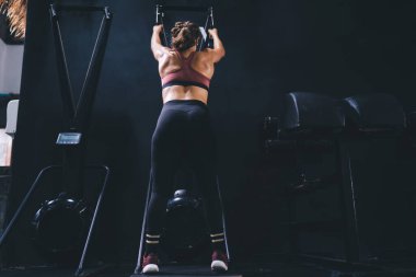 Vücut geliştirme alıştırması için spor stüdyosundaki spor simülatöründe egzersiz yapan kaslı bayan sporcuların arka plandaki görüntüsü.