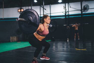 Spor salonu içinde spor kıyafetleri halter ekipmanında güçlü kararlı bir kadın spor stüdyosunun içinde spor yaparken halter kaldırıyor, beyaz kadın vücut geliştirici çapraz formda enerji ve motivasyon hissediyor.