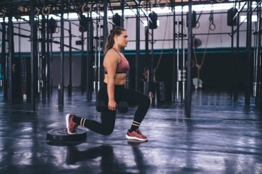 Spor giyim sektöründe atletik bir kadın zihinsel olarak sağlıklı yaşam tarzını koruyor spor salonunda egzersiz yaparken çömelme egzersizi yapıyor, halterli bir kadın kalp aktivitesi sırasında ısınıyor.