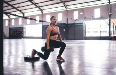 Eşofmanlı kadın, sağlıklı yaşam tarzını ve mükemmel vücut şeklini korumak için çömeliyor, halterli güçlü kadın spor salonunda zayıflıyor ve fitness hedeflerine ulaşmak için kilo veriyor.