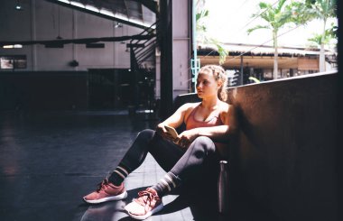 Seyyar teknolojisi olan düşünceli bir bayan atlet. Düşünceli bakışlar atıyor ve spor sonuçlarını düşünüyor. Hücresel cihazlı dalgın vücut geliştirici.