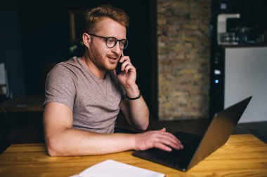 Akıllı Kafkasyalı iş adamı bilgisayarın önünde otururken akıllı telefondan arıyor. Kızıl saçlı erkek serbest internet sitesinde çalışırken cep telefonuyla konuşuyor.