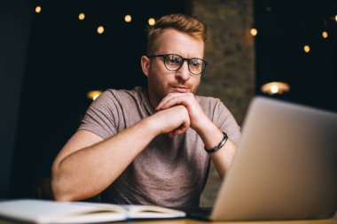Düşünceli genç adam çalışırken dizüstü bilgisayarda dikkatlice webinar izliyor. Kızıl saçlı erkek serbest yazar düşünceli bir şekilde Netbook 'ta proje çözümü üzerinde çalışıyor. Kafkas öğrenci eğitimi online