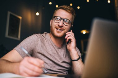 Akıllı Kafkasyalı iş adamı bilgisayarın önünde otururken akıllı telefondan arıyor. Kızıl saçlı erkek serbest internet sitesinde çalışırken cep telefonuyla konuşuyor.