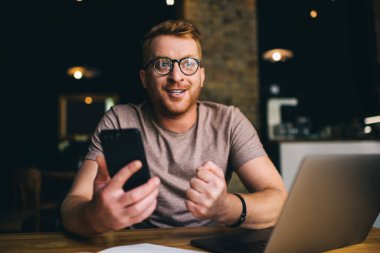 Genç başarılı adam cep telefonu kullanırken iyi bir anlaşmayı ya da başarılı bir spor bahsini kutlar. Mutlu iş adamı şanslı projeyle sevinir. Çevrimiçi yatırım sonuçları