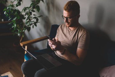 Beyaz saçlı, 30 yaşında, akıllı telefon uygulaması kullanan bir adam içeride dizüstü bilgisayar başında oturuyor. İş yerinde serbest çalışma sırasında cep telefonundan mesaj atan genç bir erkek.