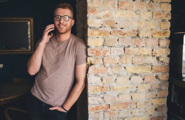 Gülümseyen ve kendine güvenen bir adamın cep telefonu konuşmasının yarım boy portresi. Beyaz, 30 yaşında, erkek, evde dururken akıllı telefondan arıyor.