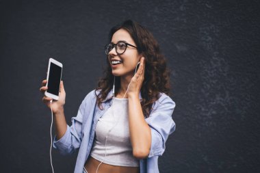 Mobil uygulamadan ses dinlerken akıllı telefon cihazıyla gülümseyen kadın dans ediyor. Kulaklıklı esmer bir kadın cep telefonunda müzik listesinin keyfini çıkarıyor. Reklam için alanı kopyala