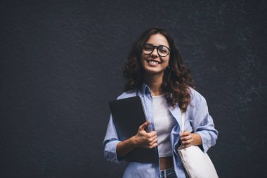 Elinde dizüstü bilgisayarla kameraya poz veren zeki bir kadının yarım boy portresi. Fotokopi alanı arkaplanının yanında duran kaygısız serbest kadın 