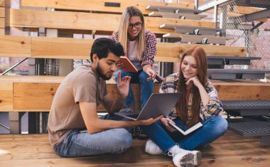 Bir grup öğrenci, kampüste dizüstü bilgisayarlarıyla otururken üniversite projesinde beyin fırtınası yapıyorlar. Üç arkadaş birlikte öğreniyor ve netbook 'ta online bilgileri tartışıyorlar.