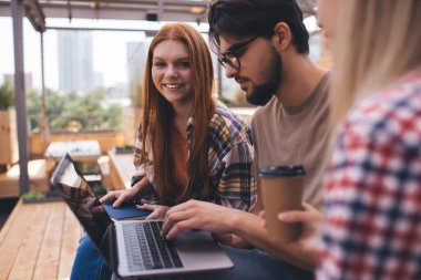 Bir grup öğrenci, kampüste dizüstü bilgisayarlarıyla otururken üniversite projesinde beyin fırtınası yapıyorlar. Üç arkadaş birlikte öğreniyor ve netbook 'ta online bilgileri tartışıyorlar.