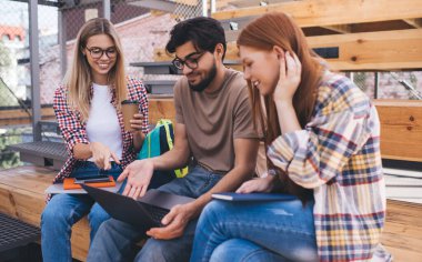 Bir grup öğrenci, kampüste dizüstü bilgisayarlarıyla otururken üniversite projesinde beyin fırtınası yapıyorlar. Üç arkadaş birlikte öğreniyor ve netbook 'ta online bilgileri tartışıyorlar.