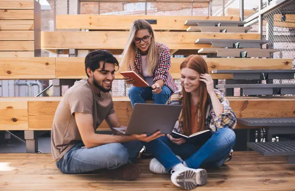 Bir grup öğrenci, kampüste dizüstü bilgisayarlarıyla otururken üniversite projesinde beyin fırtınası yapıyorlar. Üç arkadaş birlikte öğreniyor ve netbook 'ta online bilgileri tartışıyorlar.